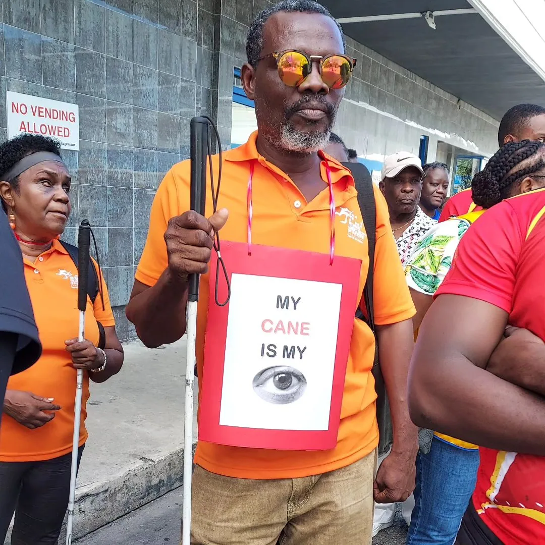 Person holding a white cane and an awareness sign reading My Cane Is My Eye