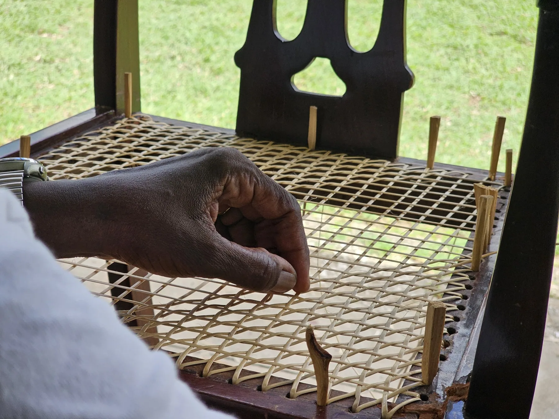 A hand carefully pulling reed through a woven chair seat