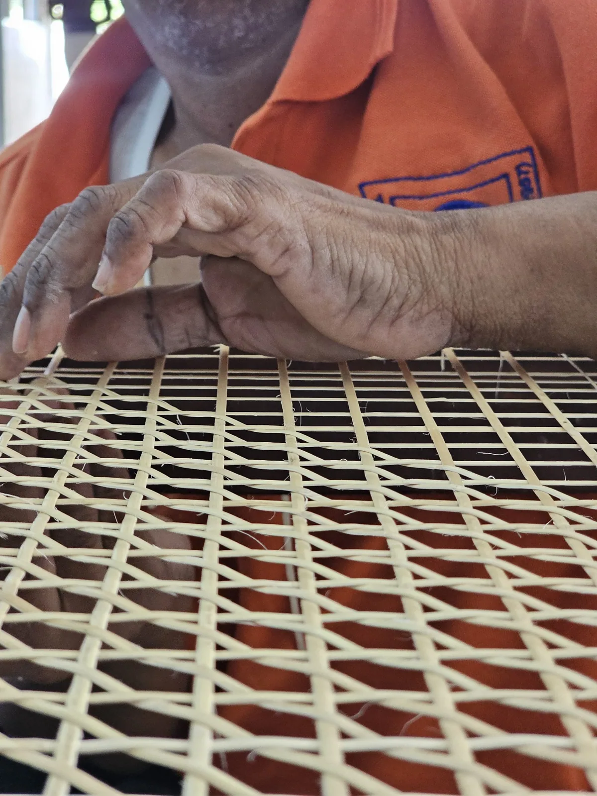 Hands manipulating cane strips on a wooden frame